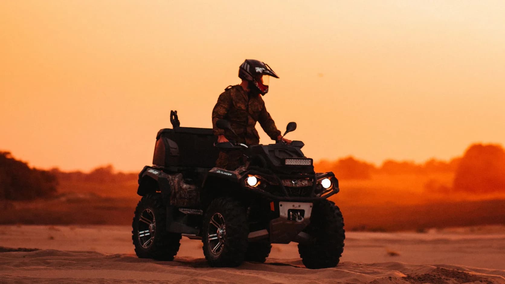 A rider on an ATV crossing sand dunes at sunset